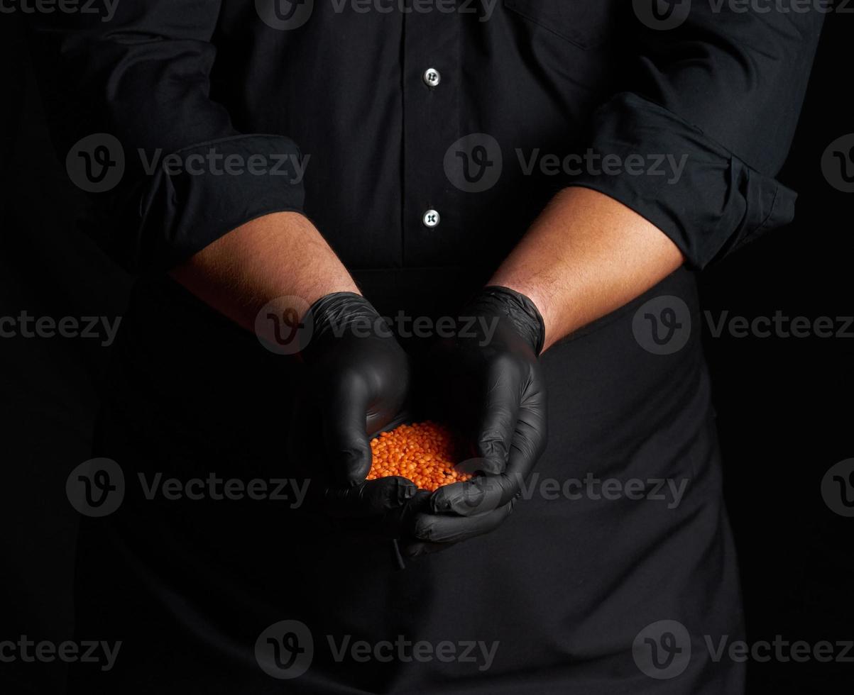 chef in black latex gloves holds raw lentils in his palms photo