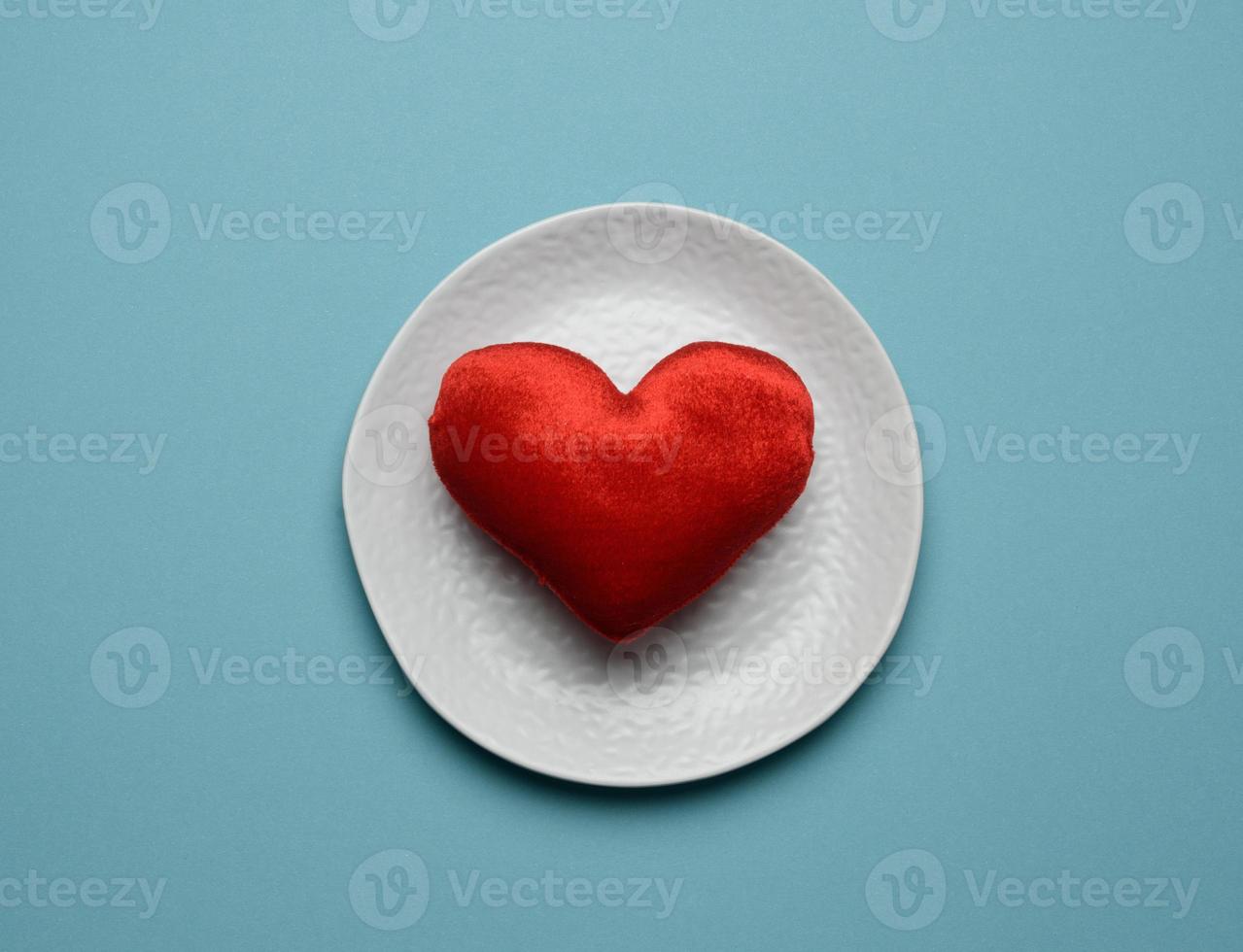 red heart lies in a white ceramic plate on a blue background photo