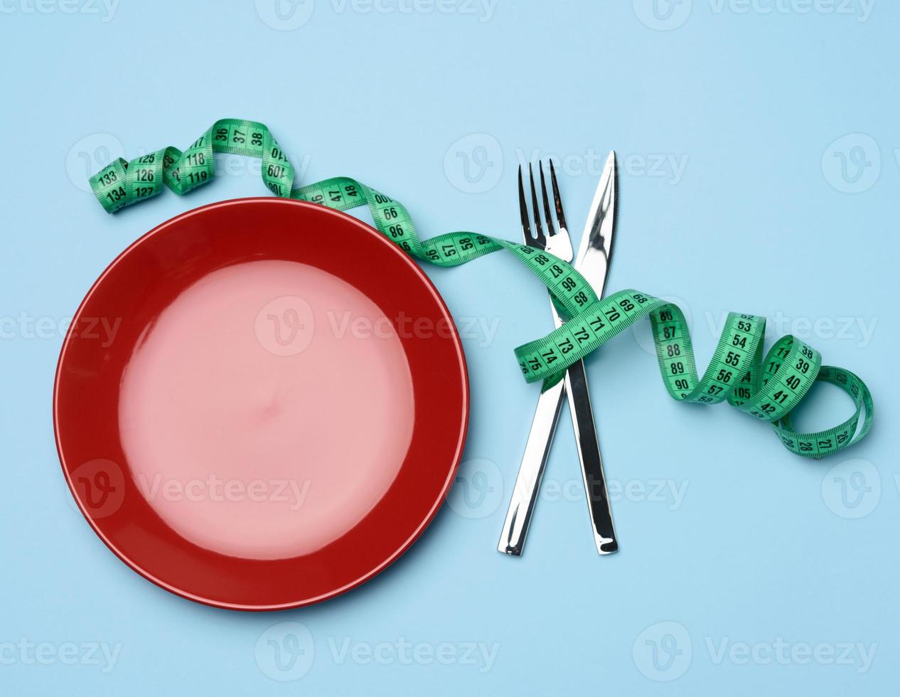 red round plate and fork and knife wrapped in green measuring tape on blue background photo