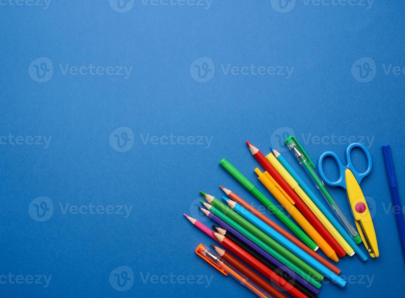 plastic scissors and multicolored wooden pencils on a blue background photo