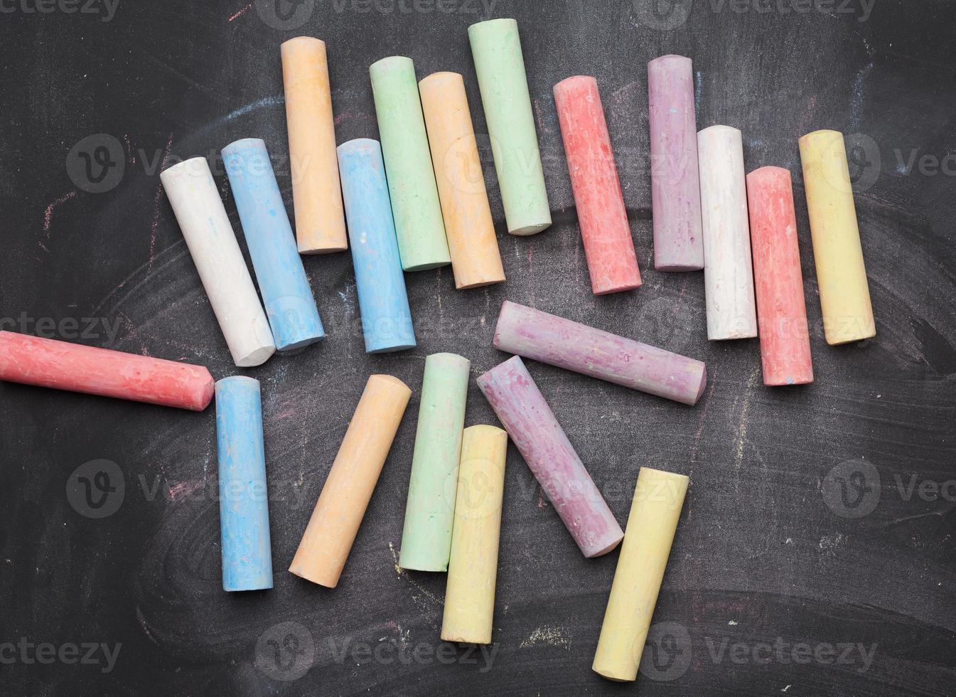 multicolored chalks on lie on empty black chalk board, top view photo