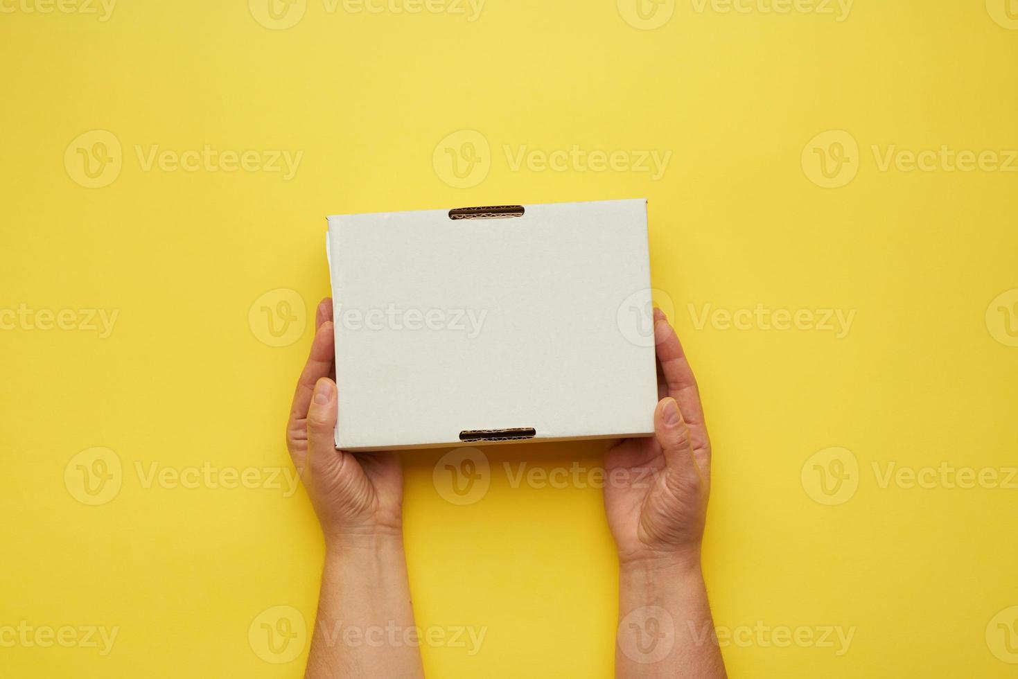 two female hands hold closed paper box on a yellow background photo
