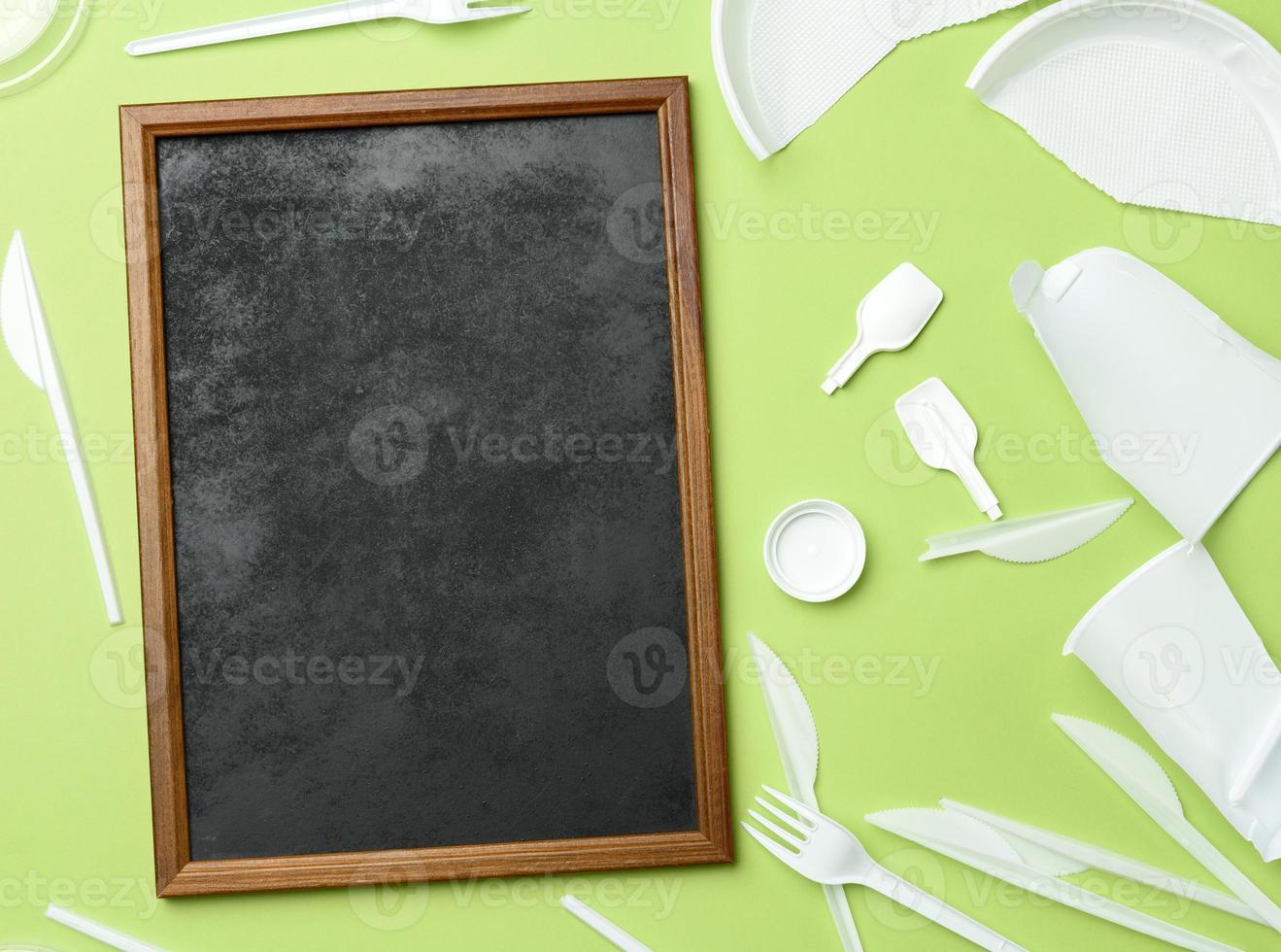 empty wooden frame and broken white plastic tableware on green background photo