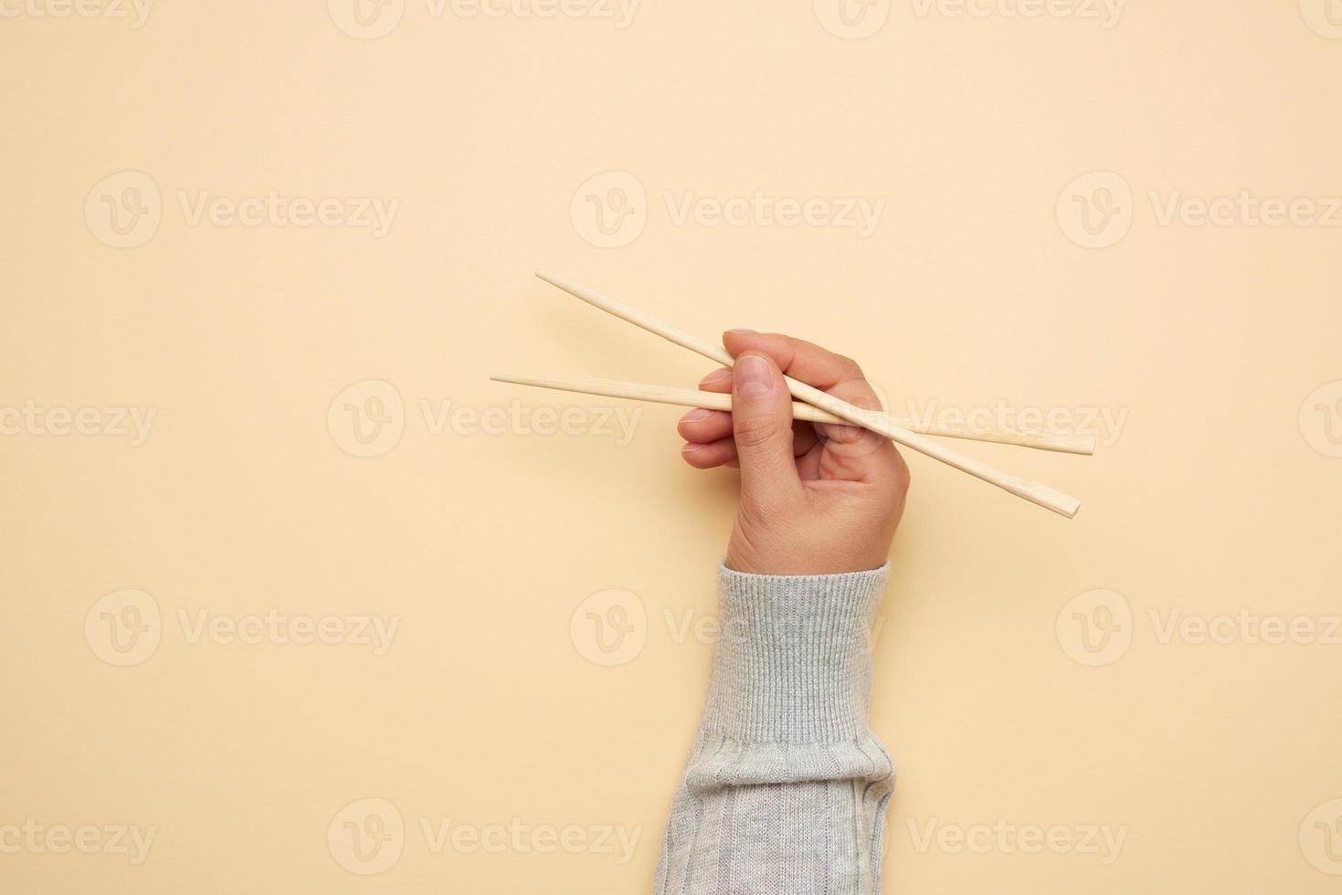 un par de palillos de madera en una mano femenina sobre un fondo beige foto