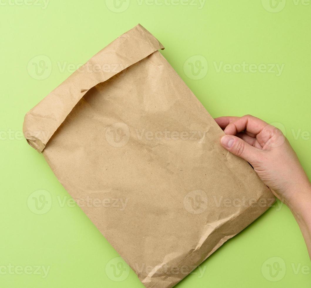 dos manos sosteniendo una bolsa de papel kraft marrón sobre un fondo verde foto