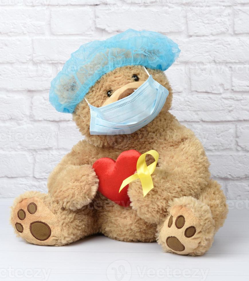 brown teddy bear holds in his paw a yellow ribbon folded in a loop photo