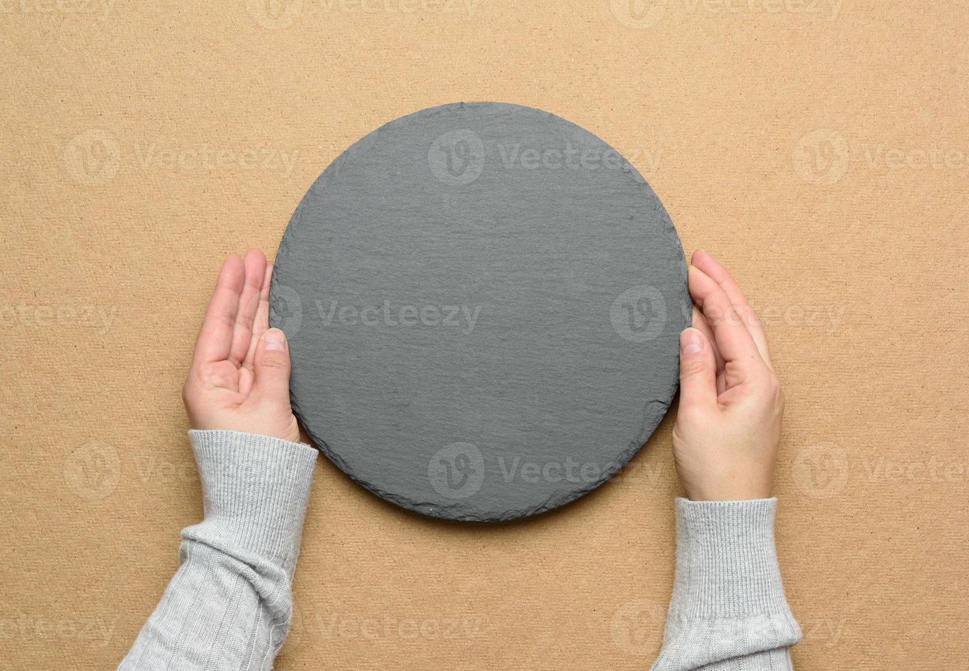hand hold empty round slate kitchen board on a brown background photo