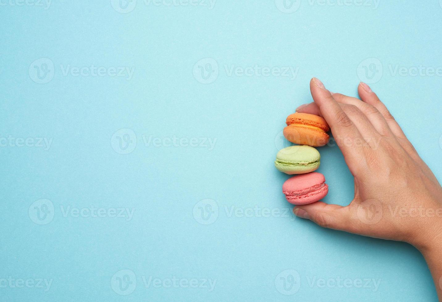 female hand holds three round baked macarons cookies on a blue background photo