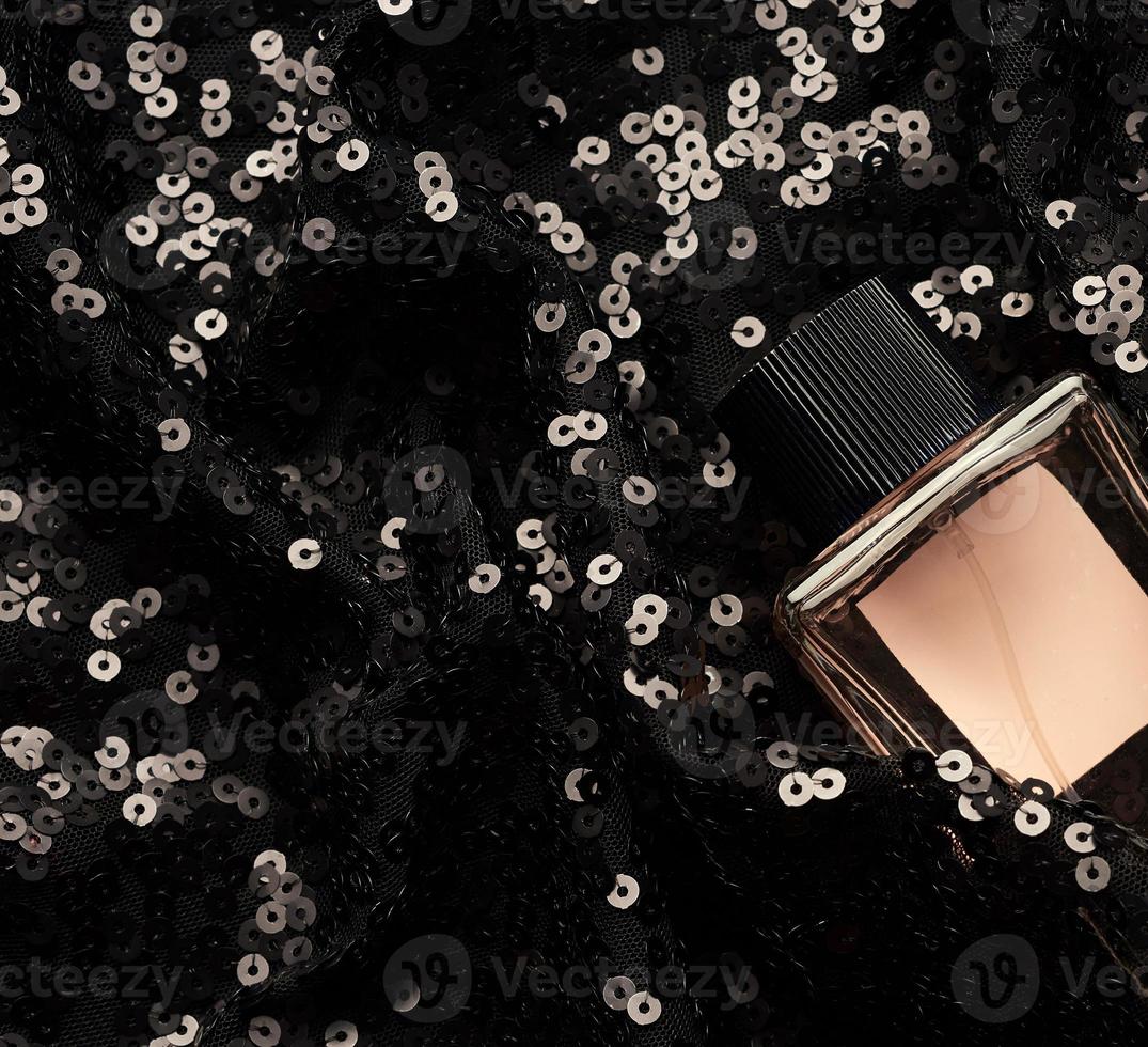 glass bottle with pink perfume liquid on black background with shiny sequins photo