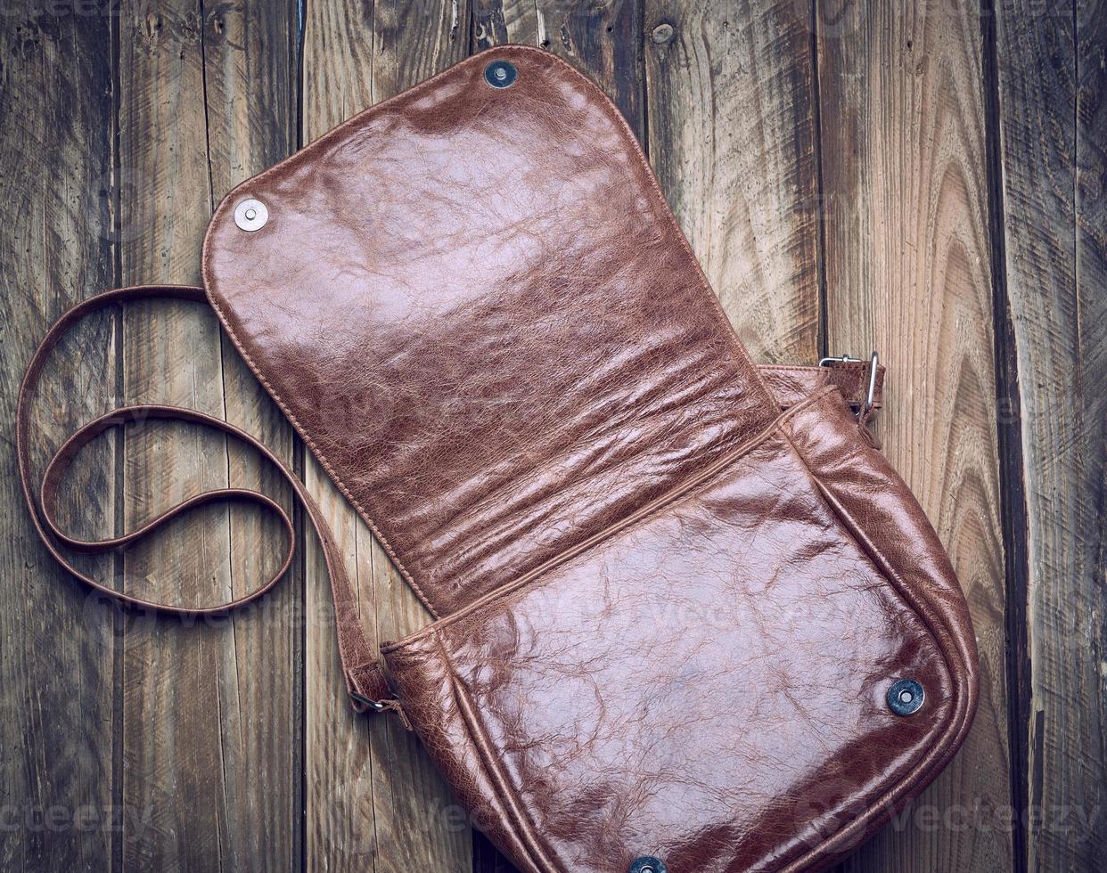 open leather brown bag with long strap on wooden background photo