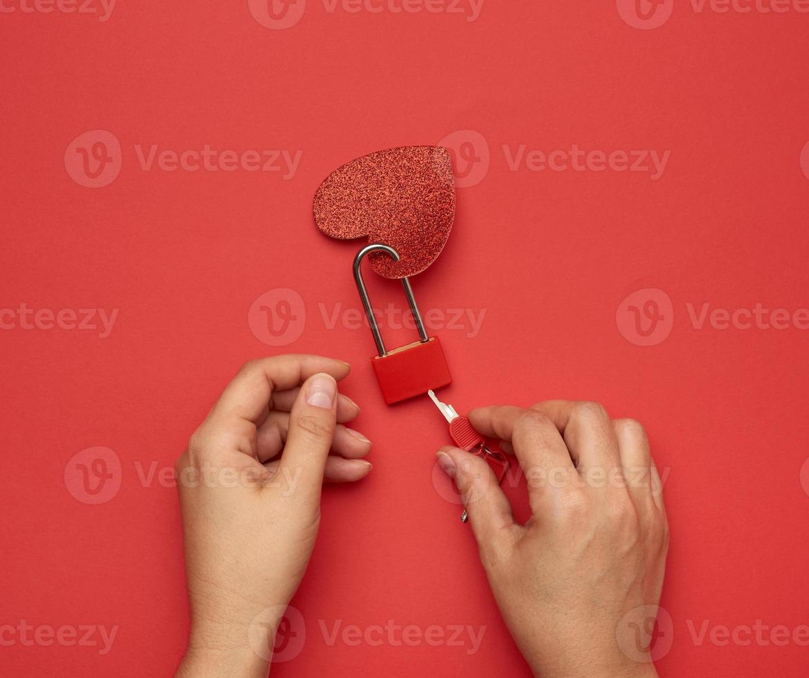 two female hands hold a metal lock and keys on a red background photo