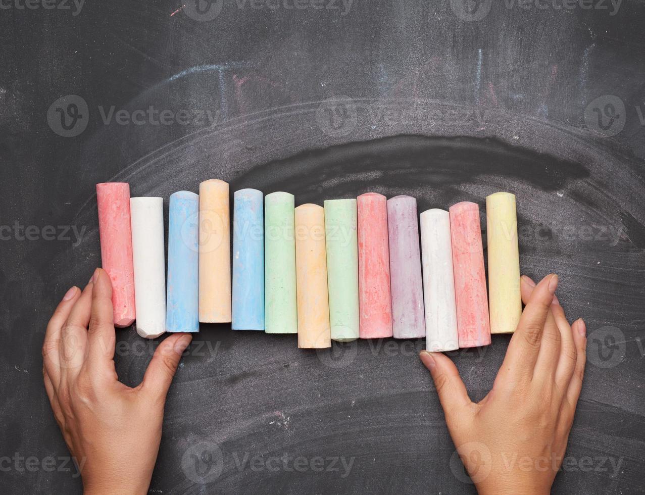 multicolored chalk on a black background and two female hands photo