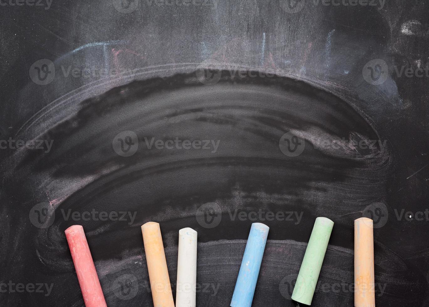 multicolored chalks on lie on empty black chalk board, top view, back to school photo