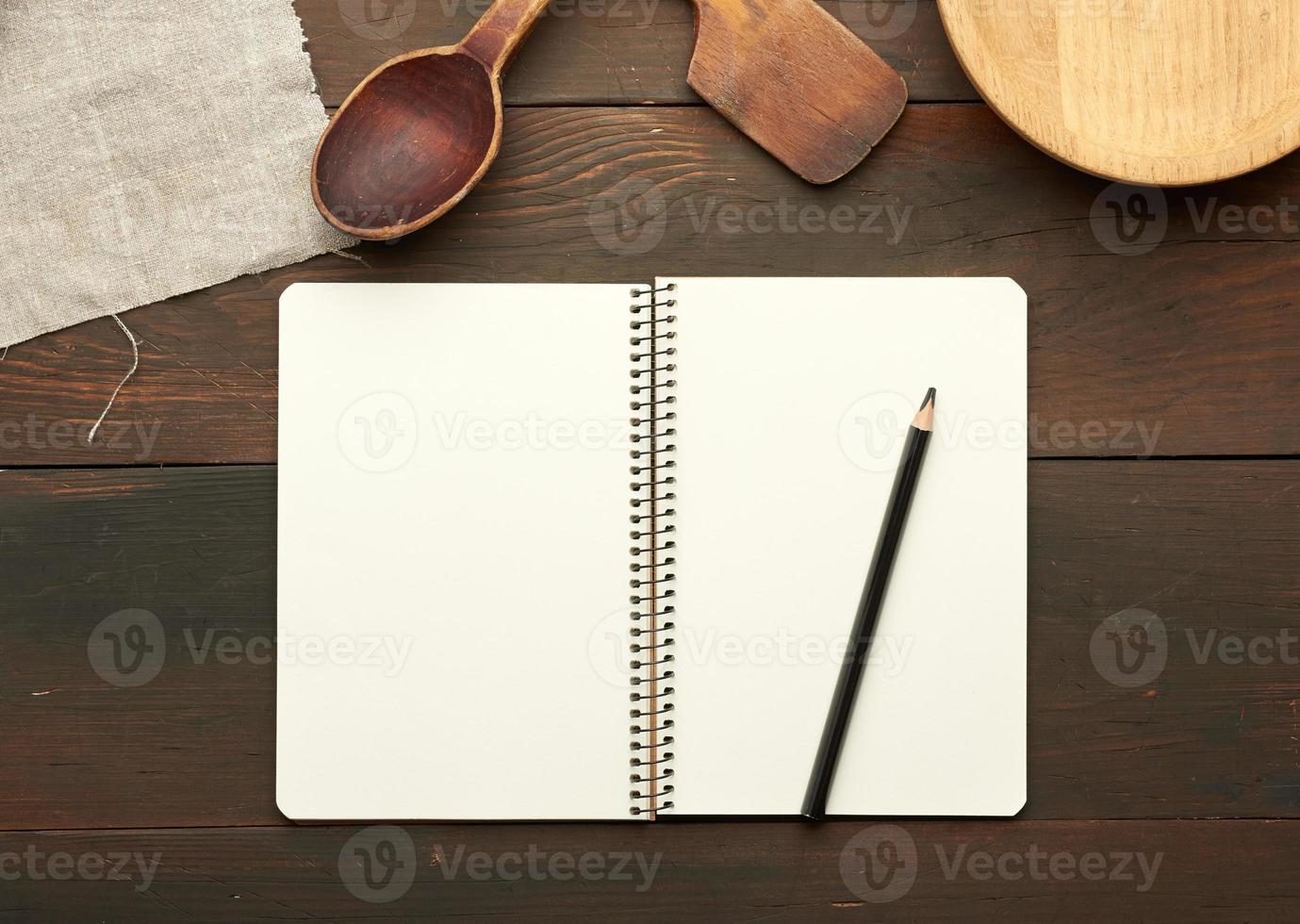 open notebook with blank white sheets and kitchen utensils on brown wooden table photo