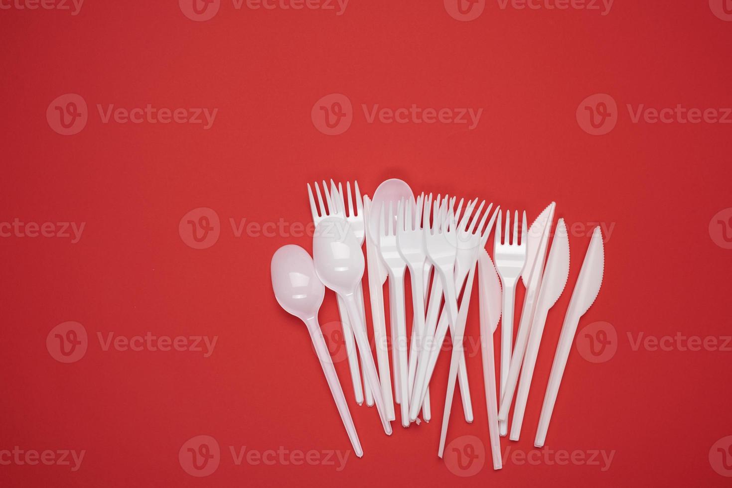 stack of plastic forks and spoons on red background, top view photo