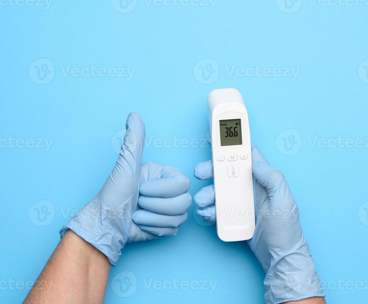 dos manos con guantes de látex azules sostienen un termómetro electrónico para medir la temperatura foto