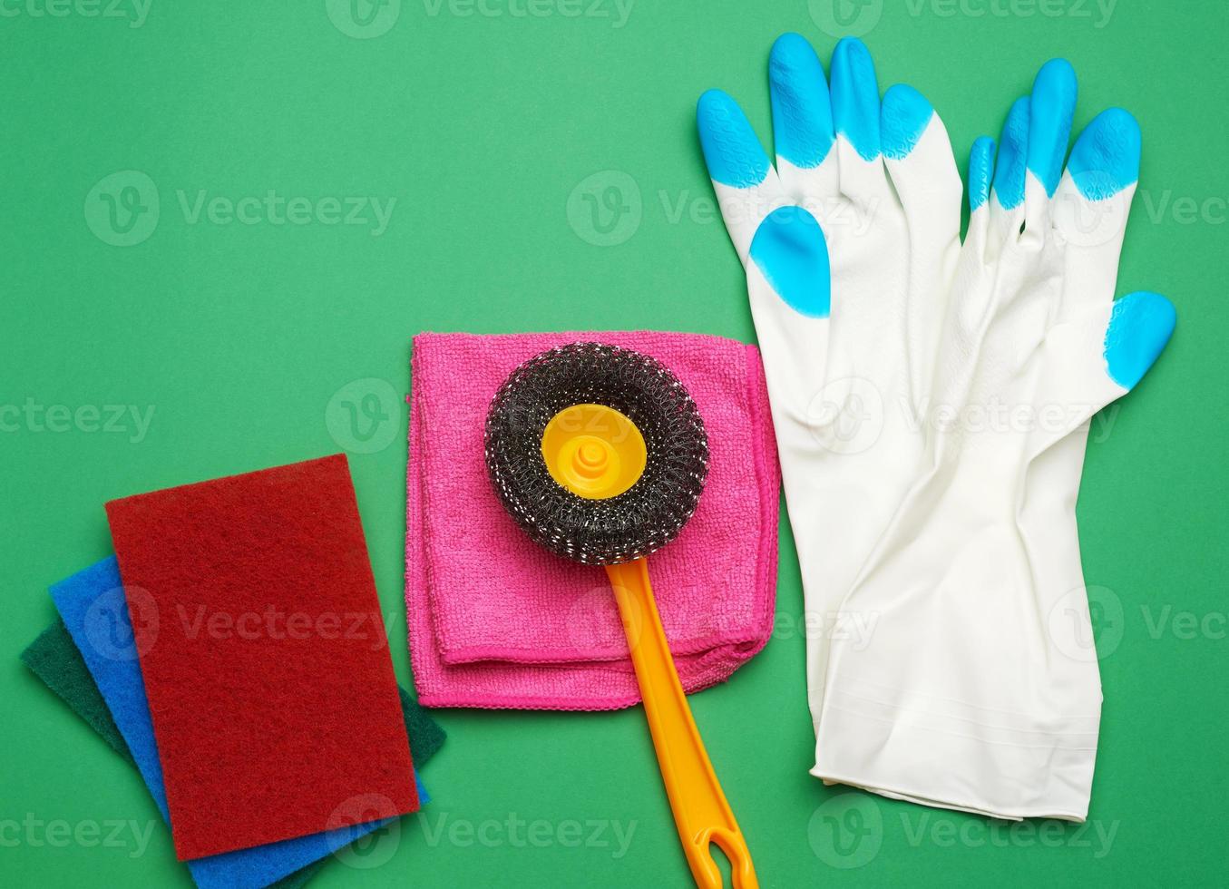 white rubber gloves for cleaning, multi-colored sponges, brushes on a green background photo