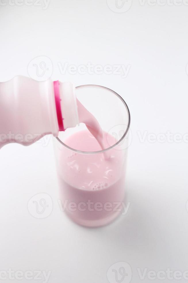Strawberry-flavored pink milk is being poured from a bottle into a glass on a white background. photo