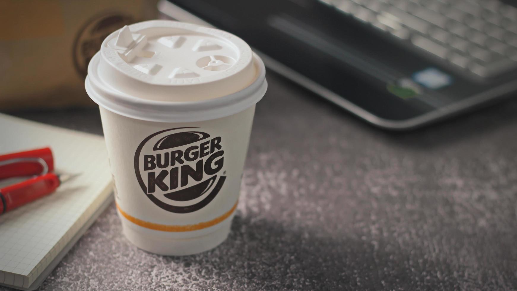 Washington, USA - January 18 2023  Coffee Cup Mug Burger King with notebook and laptop on gray table In studio lighting, Burger King is a popular food in America. photo