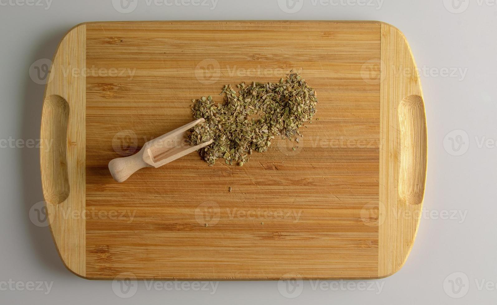 Spice oregano or marjoram. Aromatic spice for food. Background of dried oregano or marjoram on a wooden kitchen board with a measuring spoon. photo