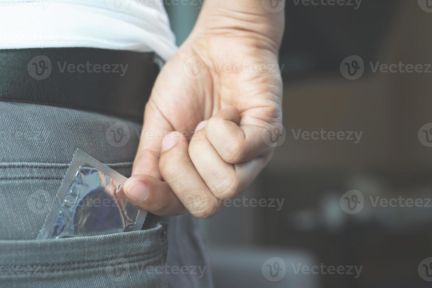 bolsillo trasero de los pantalones vaqueros del hombre joven para llevar condones tomando en la mano el condón de los pantalones vaqueros, el concepto de sexo seguro en la cama previene la infección. foto