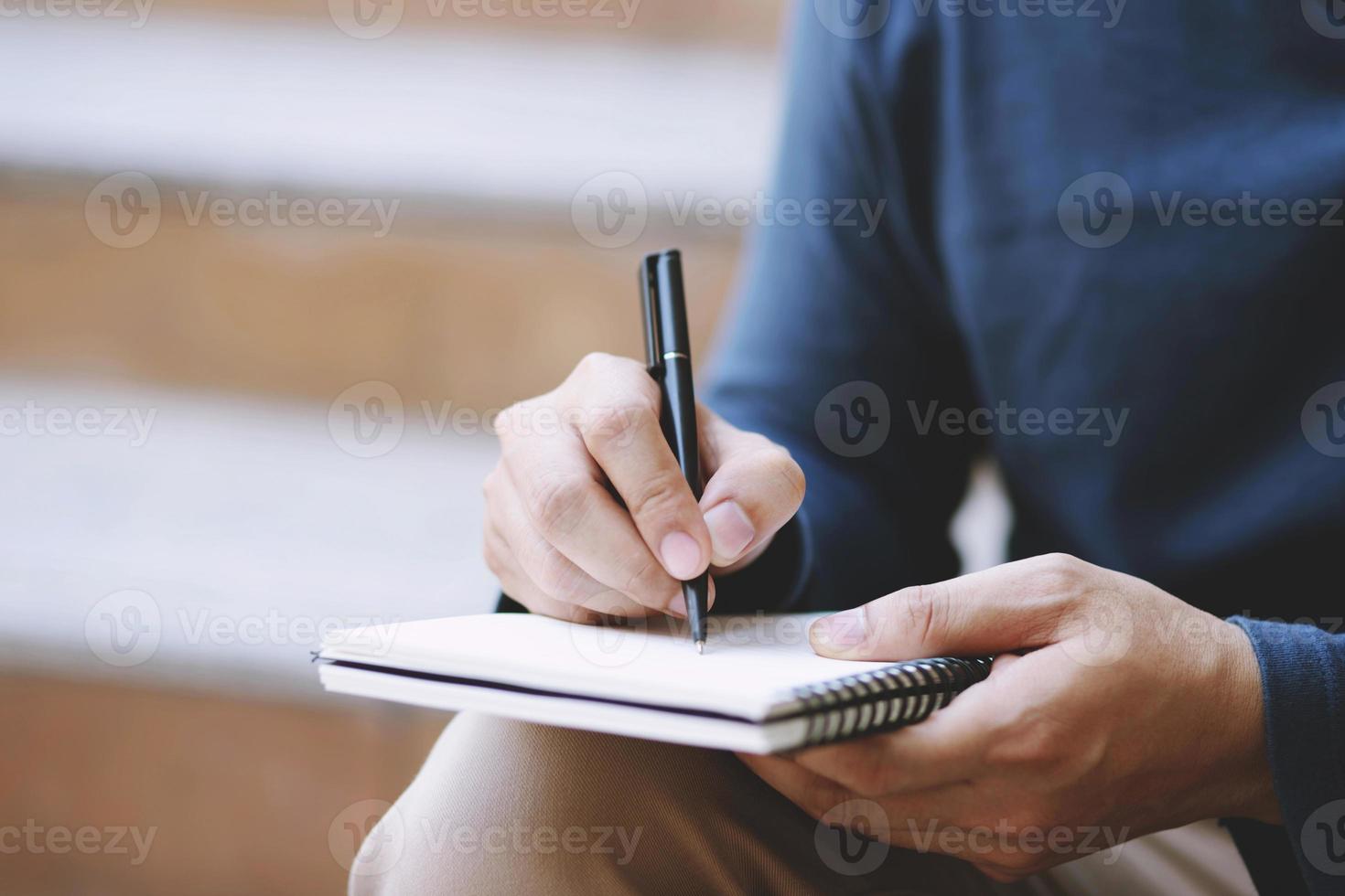 close up hand young man are sitting using pen writing Record Lecture note pad into the book on the table wood. photo
