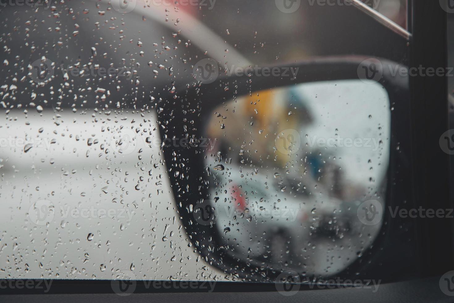 Drops Of Rain Drizzle on the glass windshield in the evening. street in the heavy rain. Bokeh Tail light and Traffic lights in city. Please drive  car carefully, slippery road. soft focus. photo