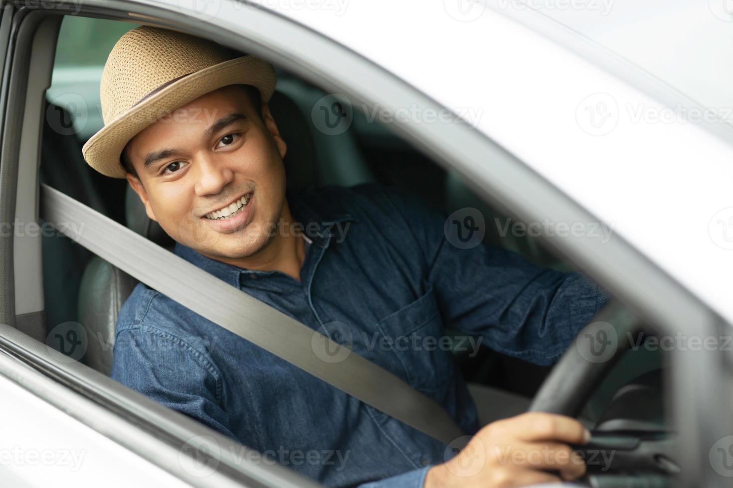 Portrait of happy smiling young asian man with fasten seat belts for safety travel on the road showing thumbs up while driving in his car. photo