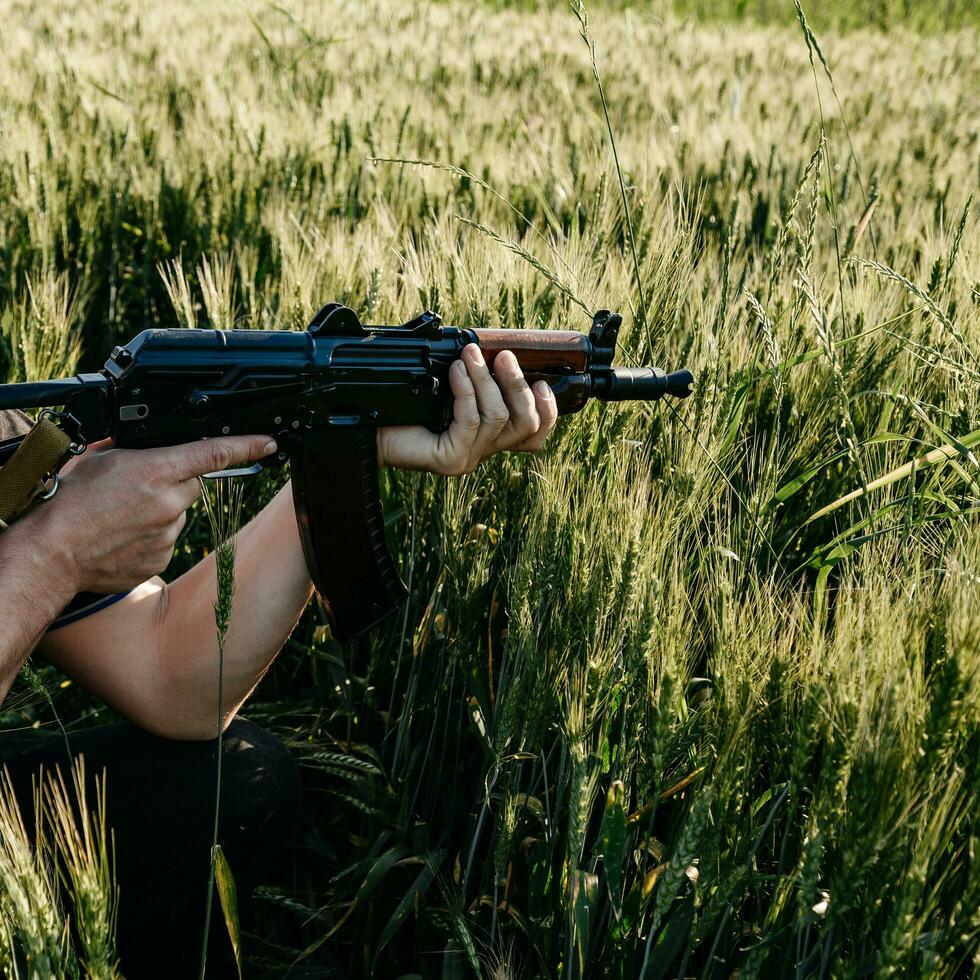 un soldado con rifles de asalto militares de combate ak 74 se encuentra en un campo, campos de trigo ucranianos y guerra. foto
