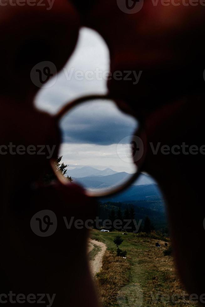 la novia y el novio sostienen un anillo en sus labios, las montañas se pueden ver a través del anillo. foto