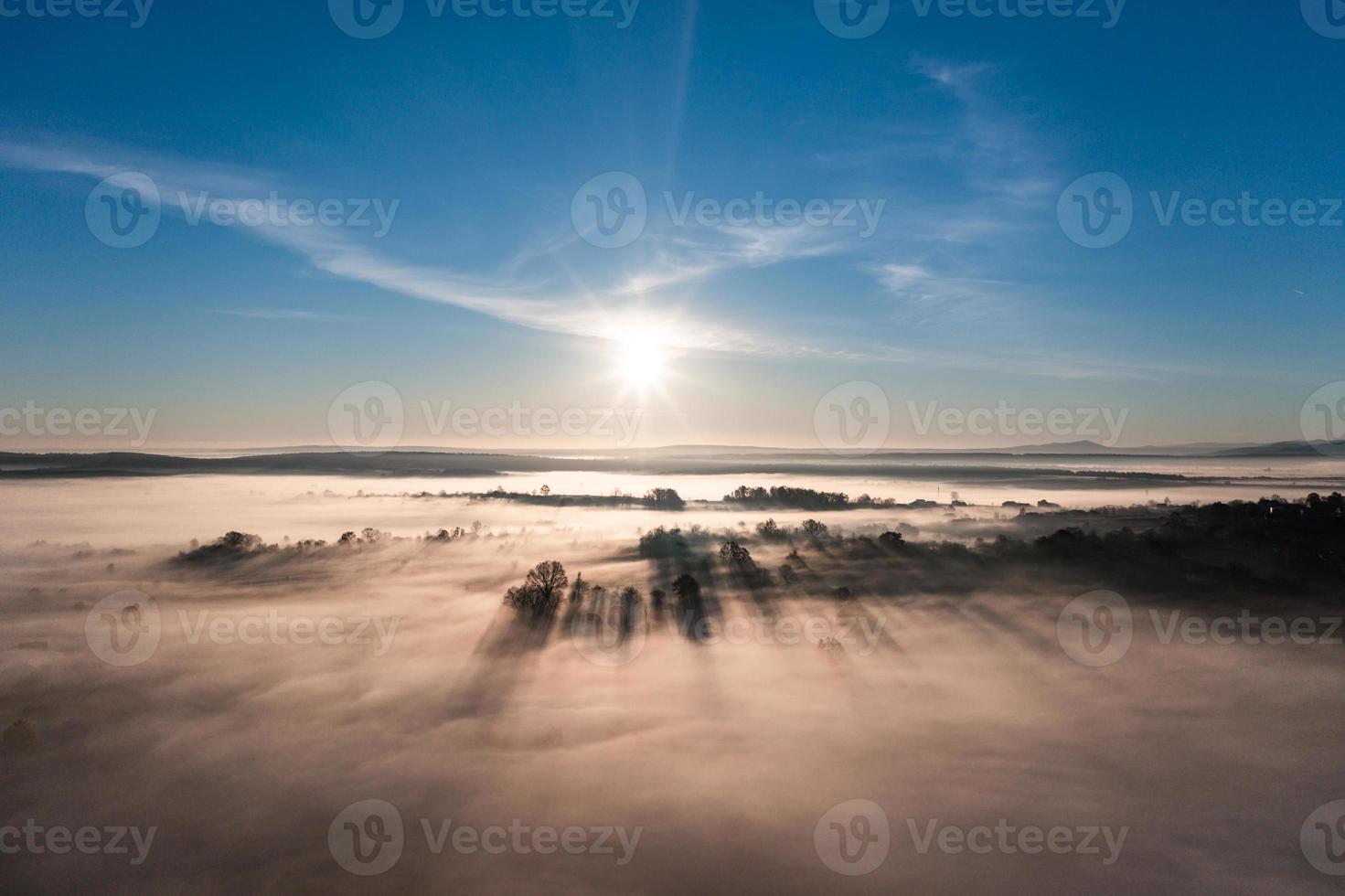Flying over a village at dawn, bright sun on the horizon and fog over a small village. photo