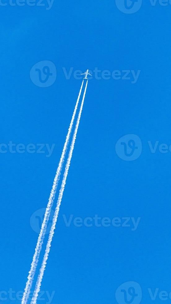 Two engined airplane during flight in high altitude with condensation trails photo