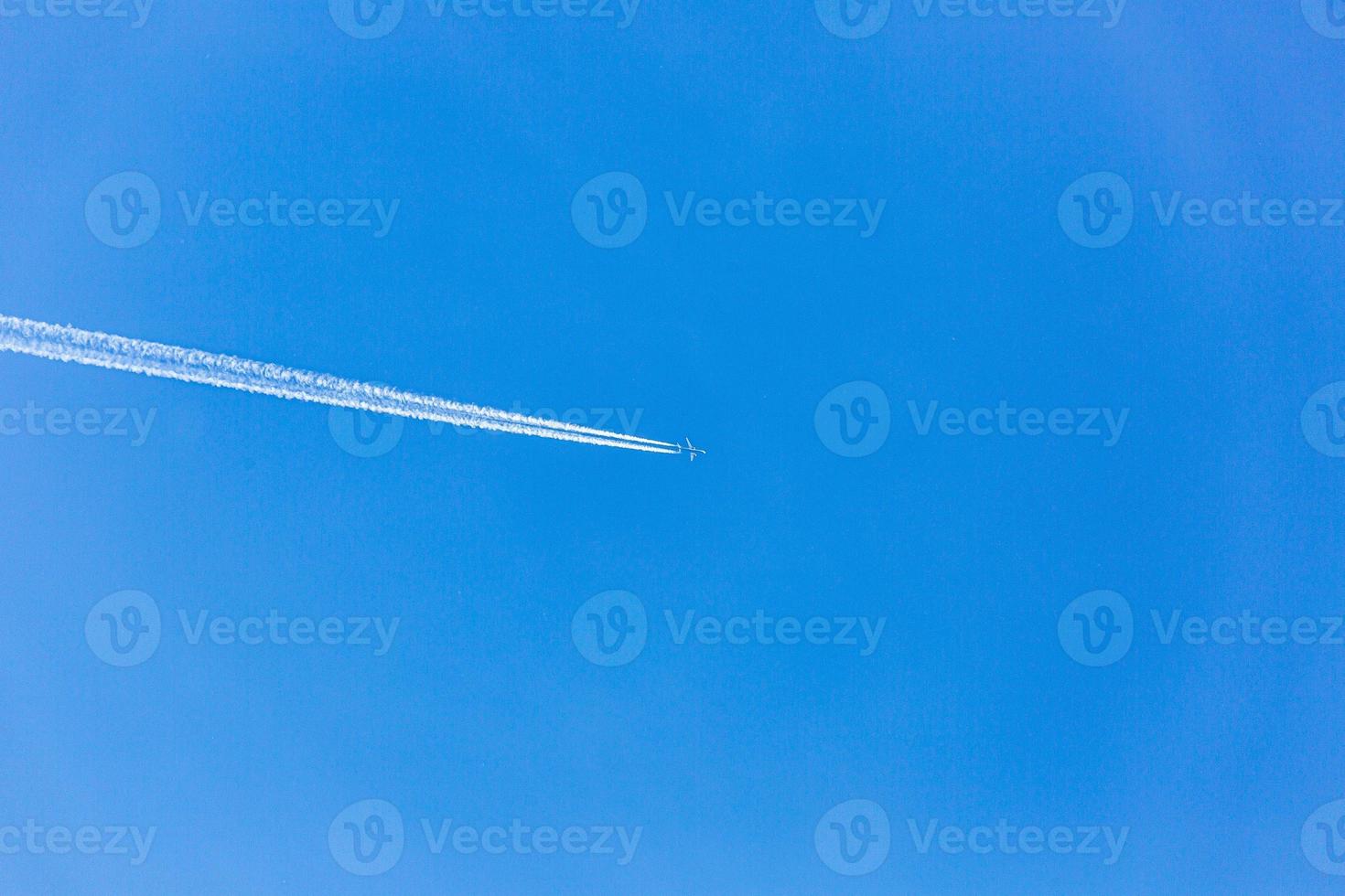 Two engined airplane during flight in high altitude with condensation trails photo