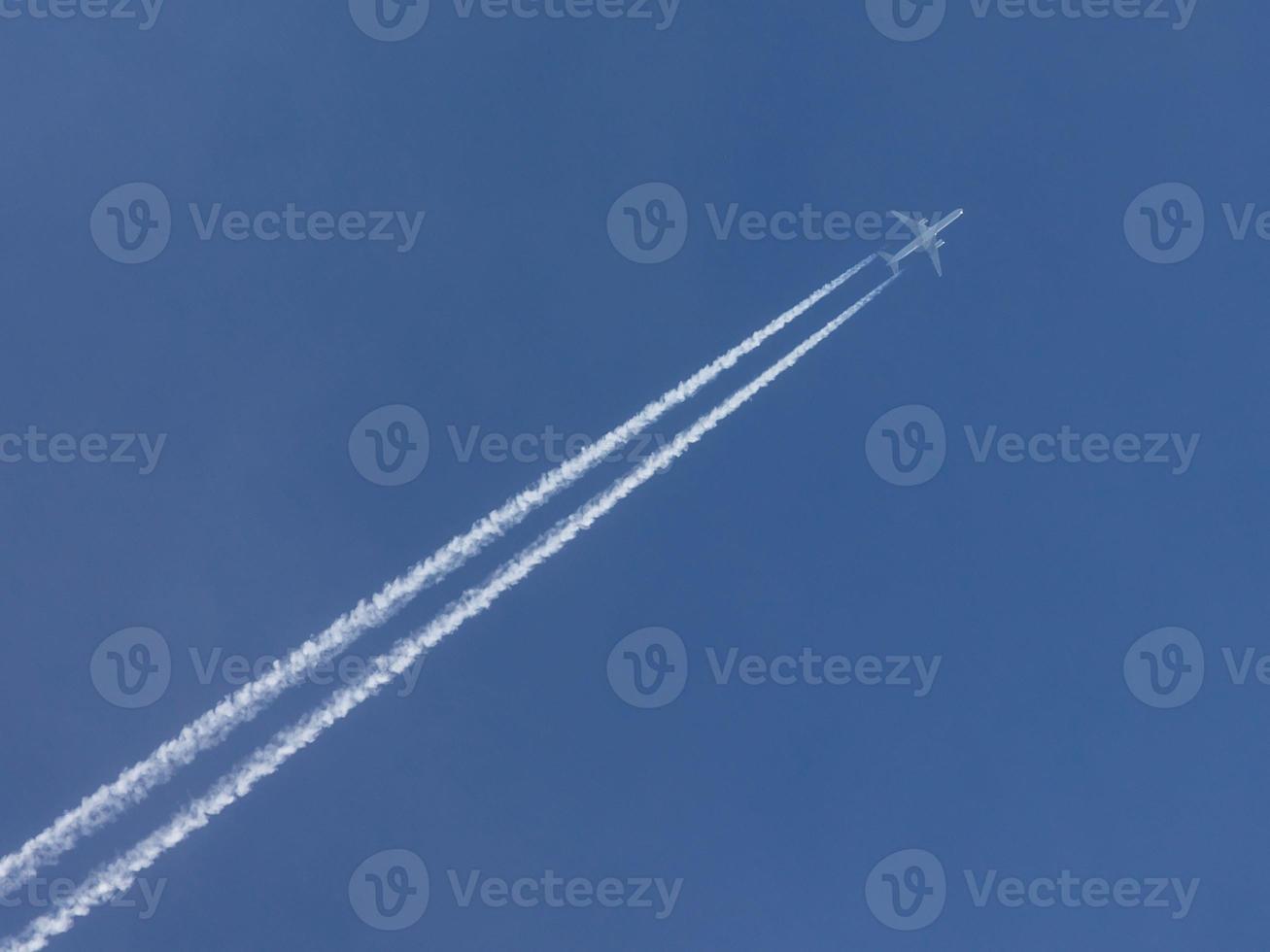 Airplane with condensation trail in blue sky photo