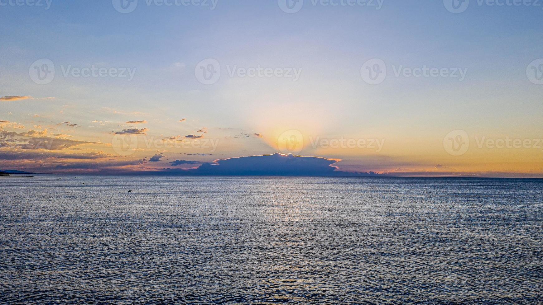 Image of sunrise over the sea hidden by clouds with intense colors and sun rays photo