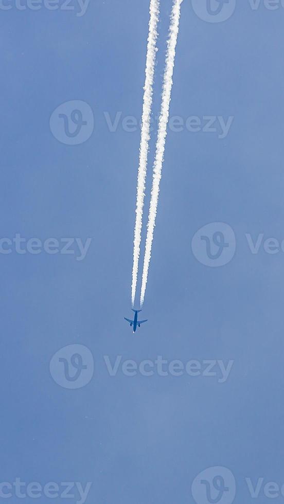Two engined airplane during flight in high altitude with condensation trails photo