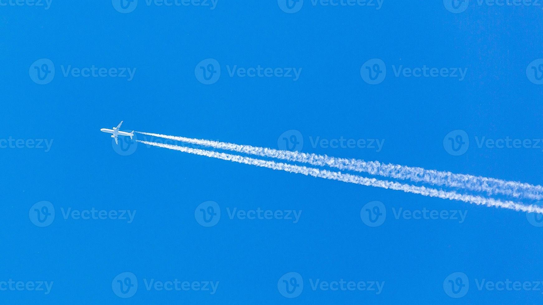Two engined airplane during flight in high altitude with condensation trails photo