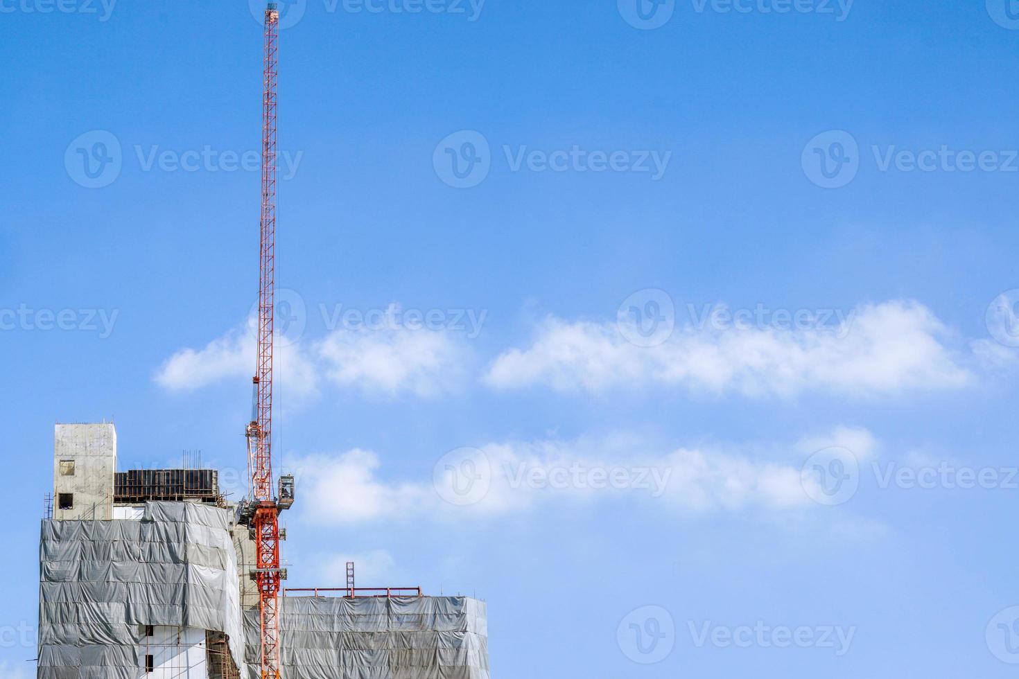 Building under construction with hoisting cranes on bright blue sky background photo