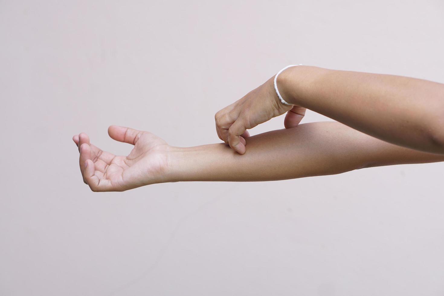 Woman scratching arm from itching on light gray background. Cause of itchy skin include insect bitesConcept of health care skin photo