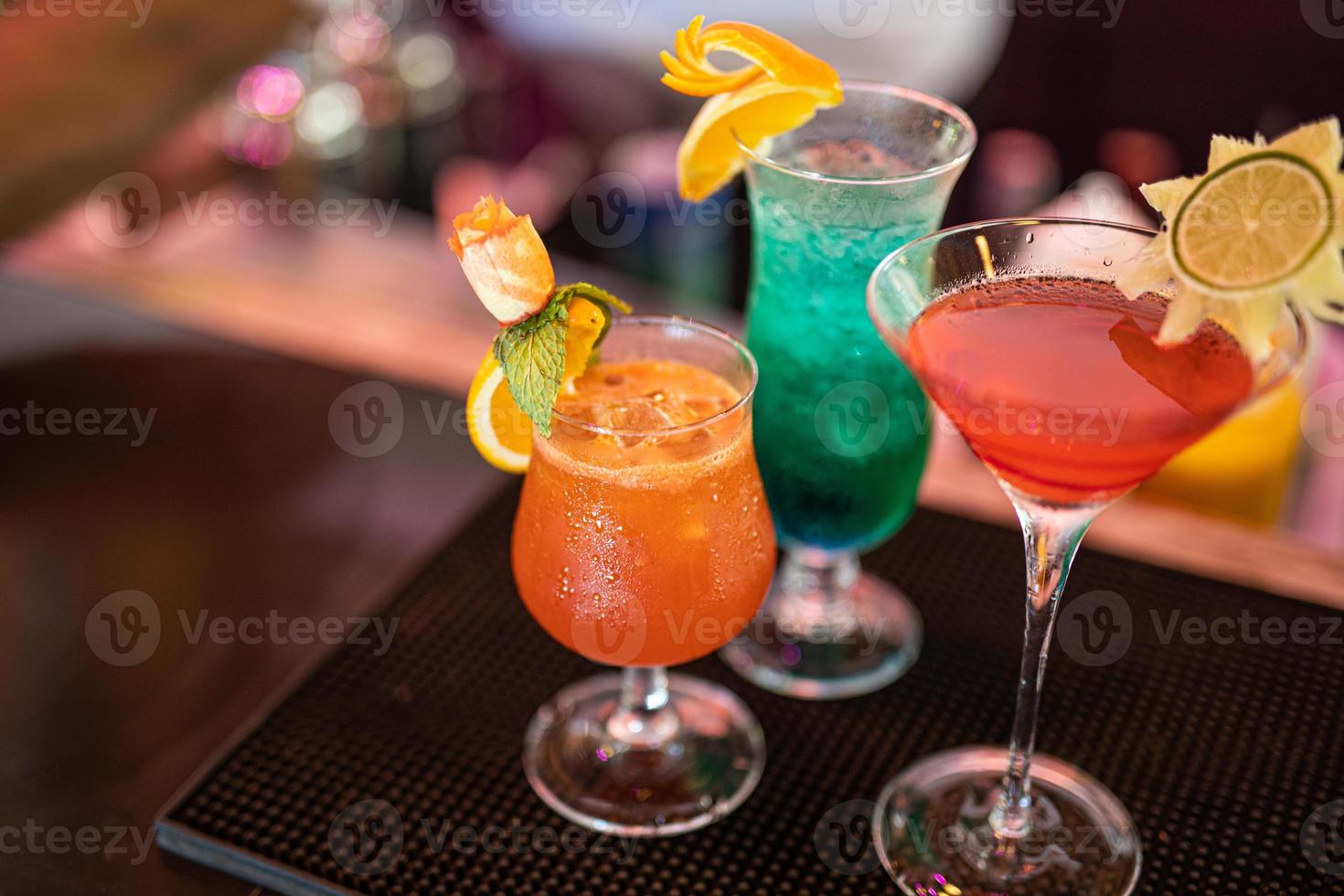 Exotic cocktails, mojito cocktail, orange cocktail, strawberry cocktail in glass glasses with straws and fruits and blurred bar accessories shaker, spoon, spices Colorful cocktails on the bar counter photo