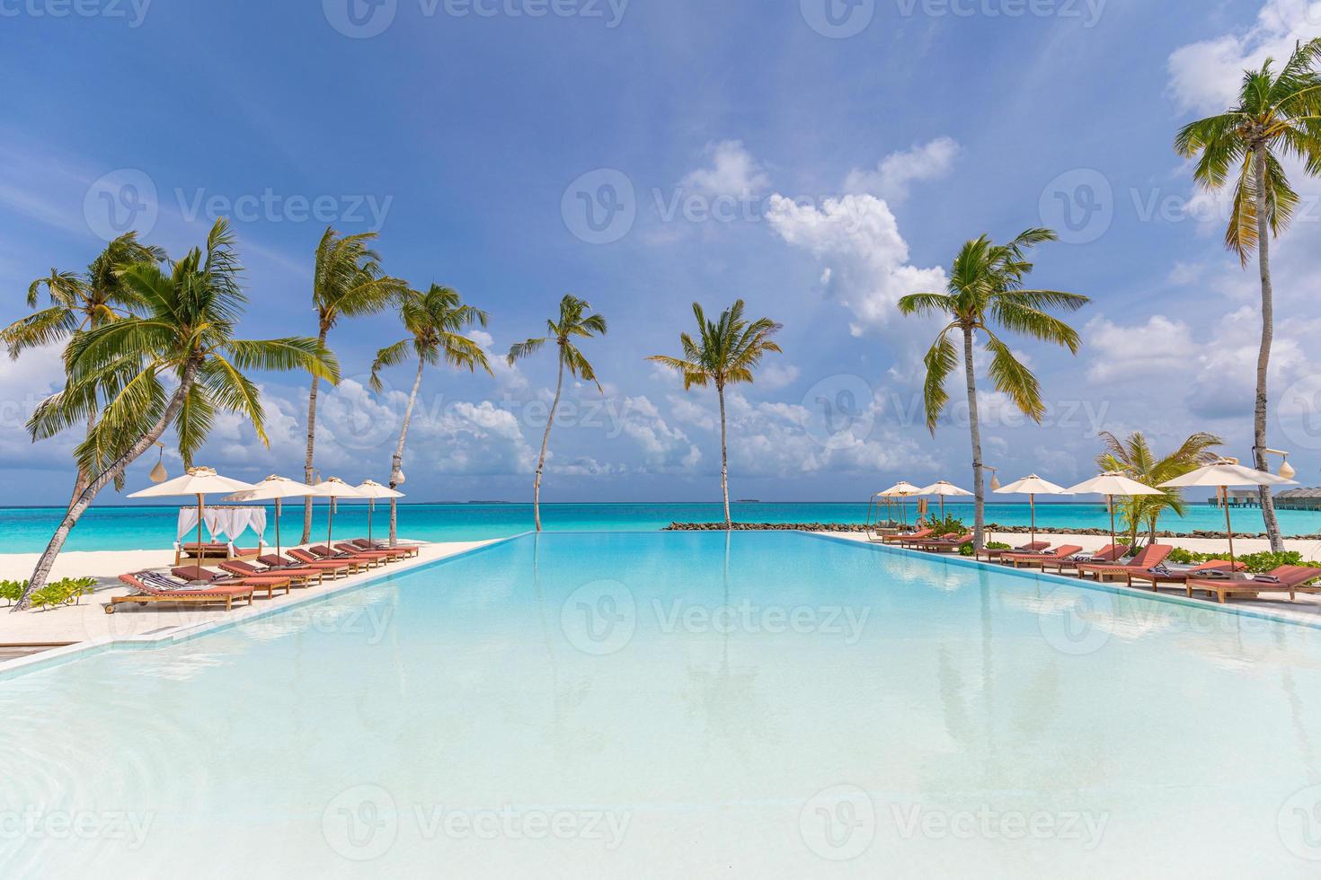 Tranquil seaside pool, relax chaise lounge concept in luxury resort in Maldives, Indian Ocean. Amazing beach view, chairs umbrellas endless infinity pool, ocean view leisure lifestyle. Summer vacation photo