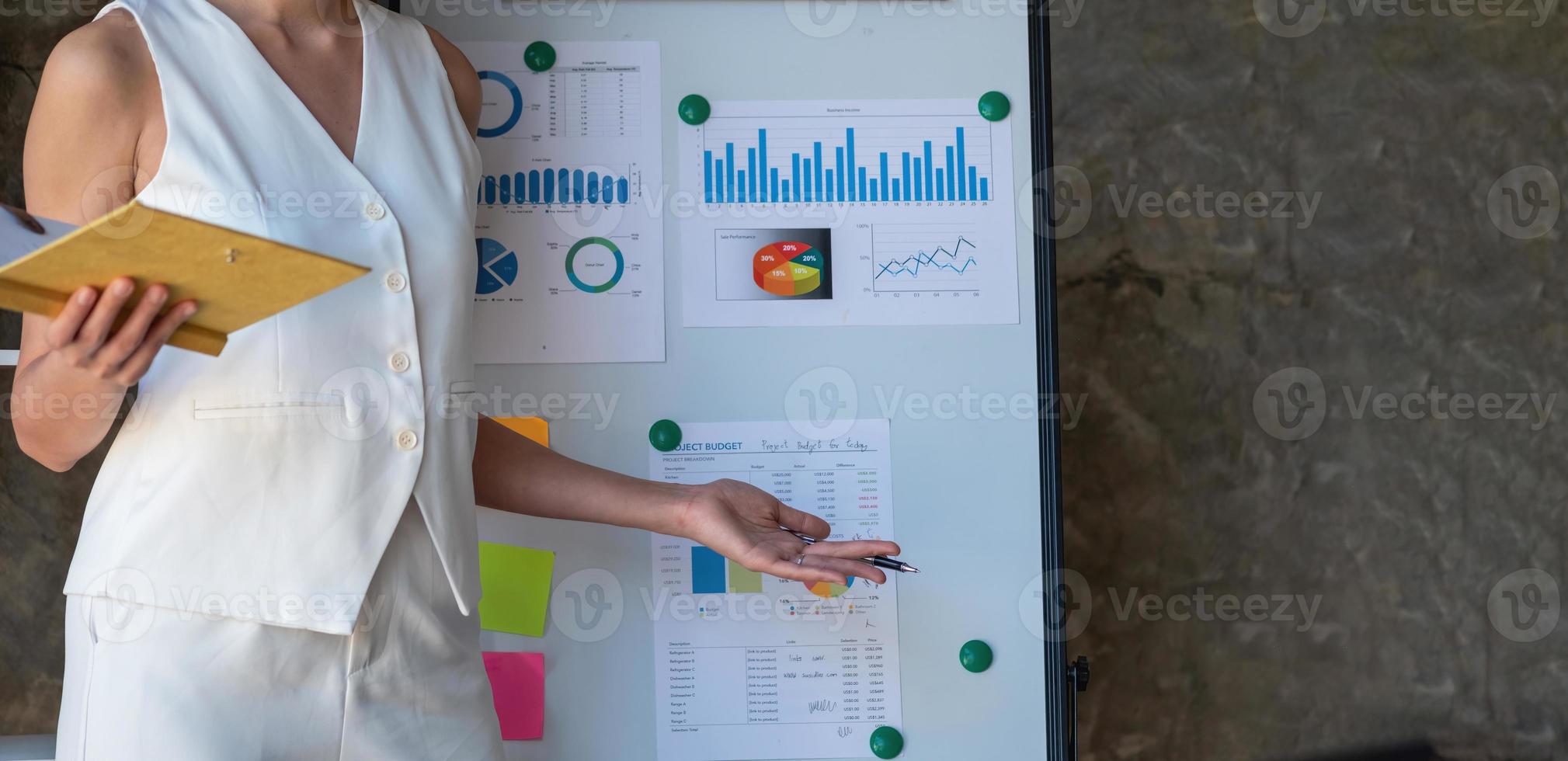 mujer de negocios asiática que presenta datos comerciales con un tablero con gráficos, gráficos a mano sosteniendo un cuaderno amarillo y documentos comerciales sobre la mesa en la oficina, concepto comercial. foto