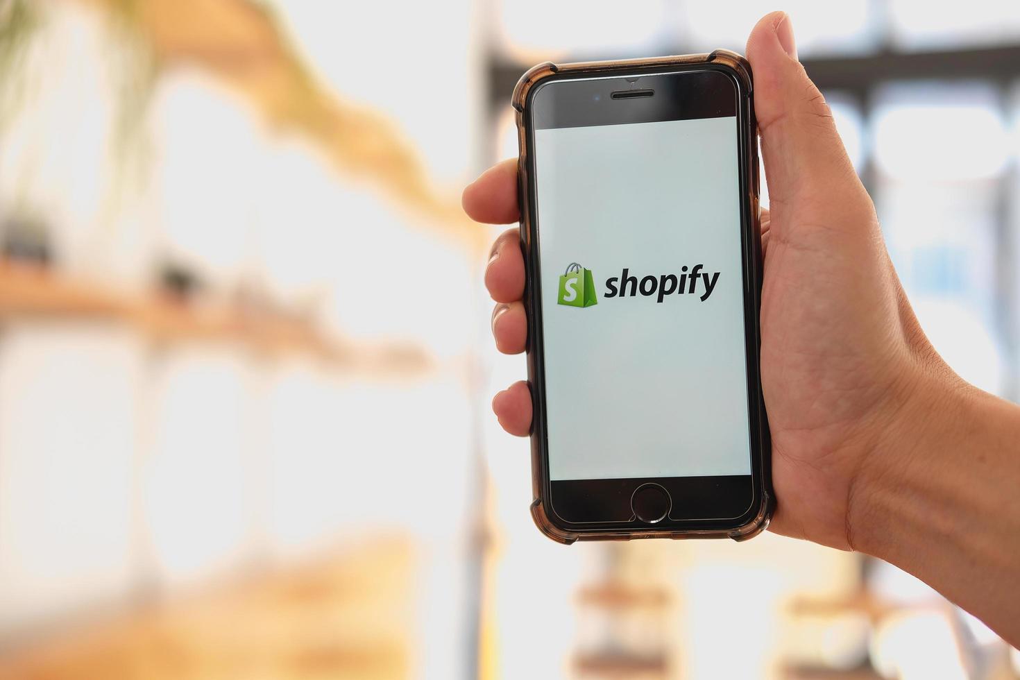 chiang mai, tailandia - 13 de enero de 2023 - una mujer sostiene un teléfono móvil iphone 8 plus con la aplicación shopify en la pantalla en una panadería y cafetería. Shopify es una plataforma de comercio electrónico para tiendas en línea. foto