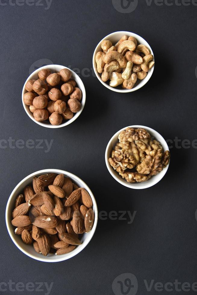 A set of nuts in white cups on a black background. Peanuts, hazelnuts and almonds. Walnut. A delicious set of nuts. photo