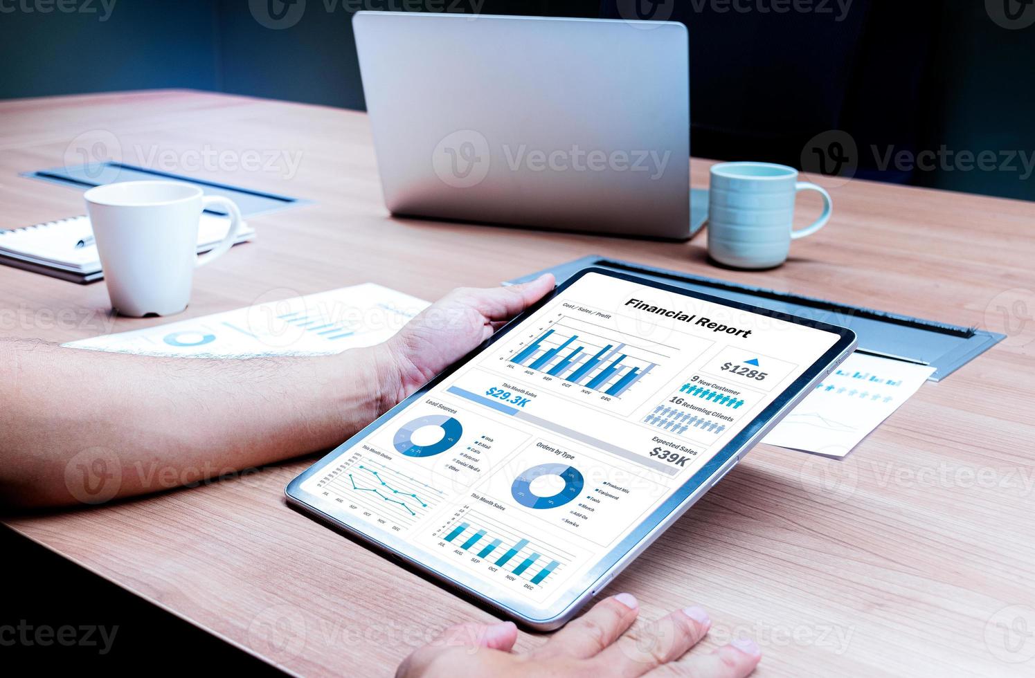 Businessman hand holding tablet with mock up financial report slide show presentation on display in meeting with laptop and coffee cup on table background photo