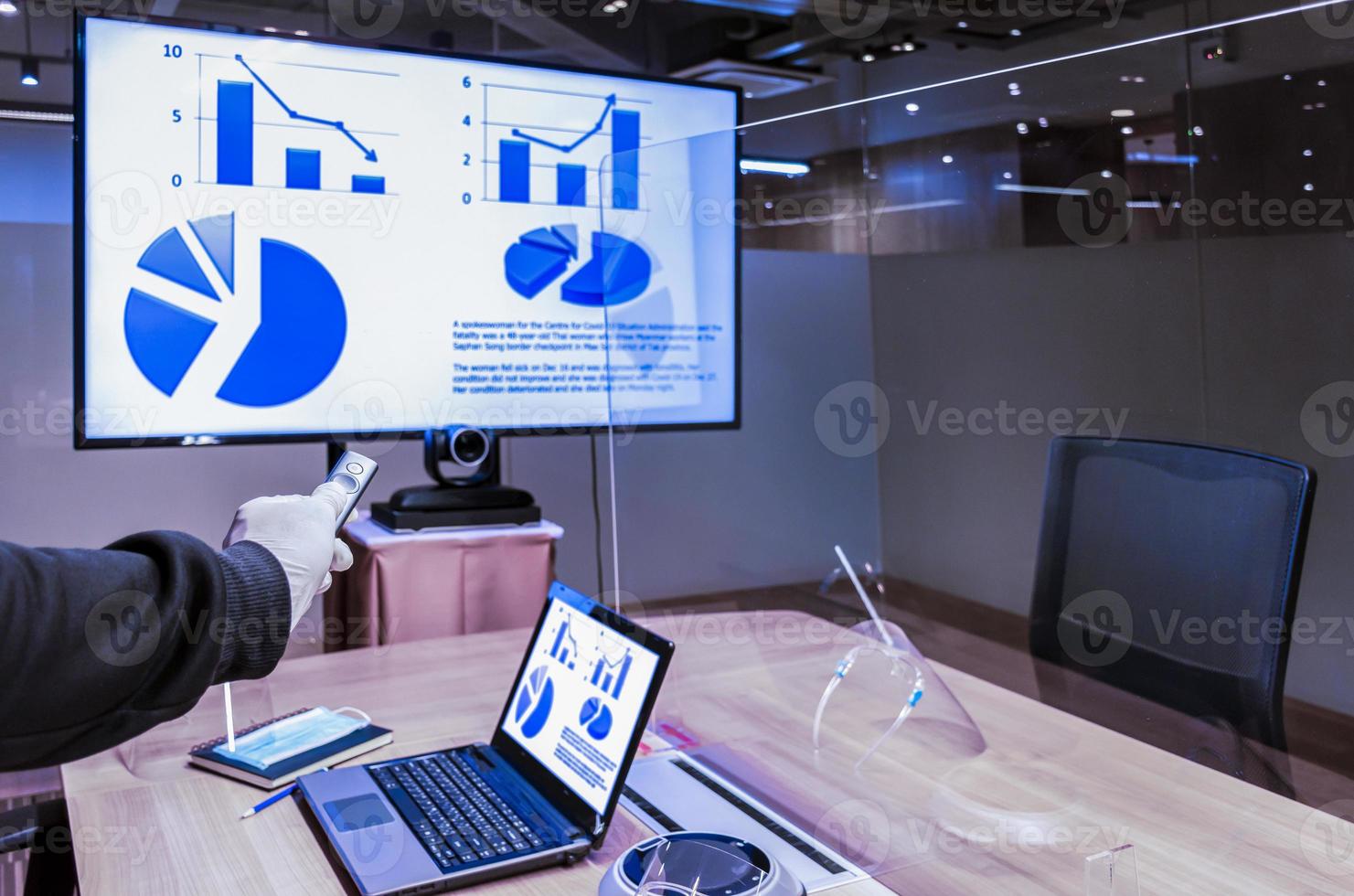 Businessman hand hold remote control with slide presentation on display television and laptop in meeting room photo