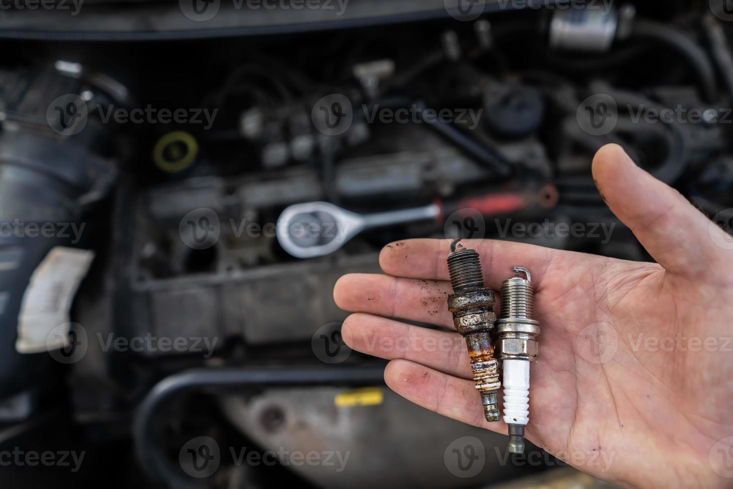 old and new spark plug in the hands of a mechanic on the background of a car engine photo