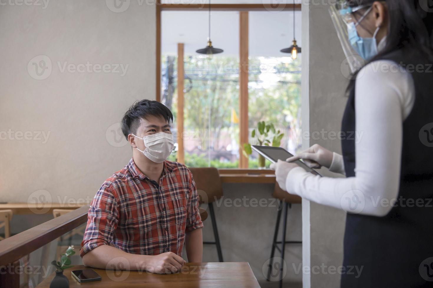 Businessman customer sitting play smartphone waiting for receiving coffee from waitress with face mask photo