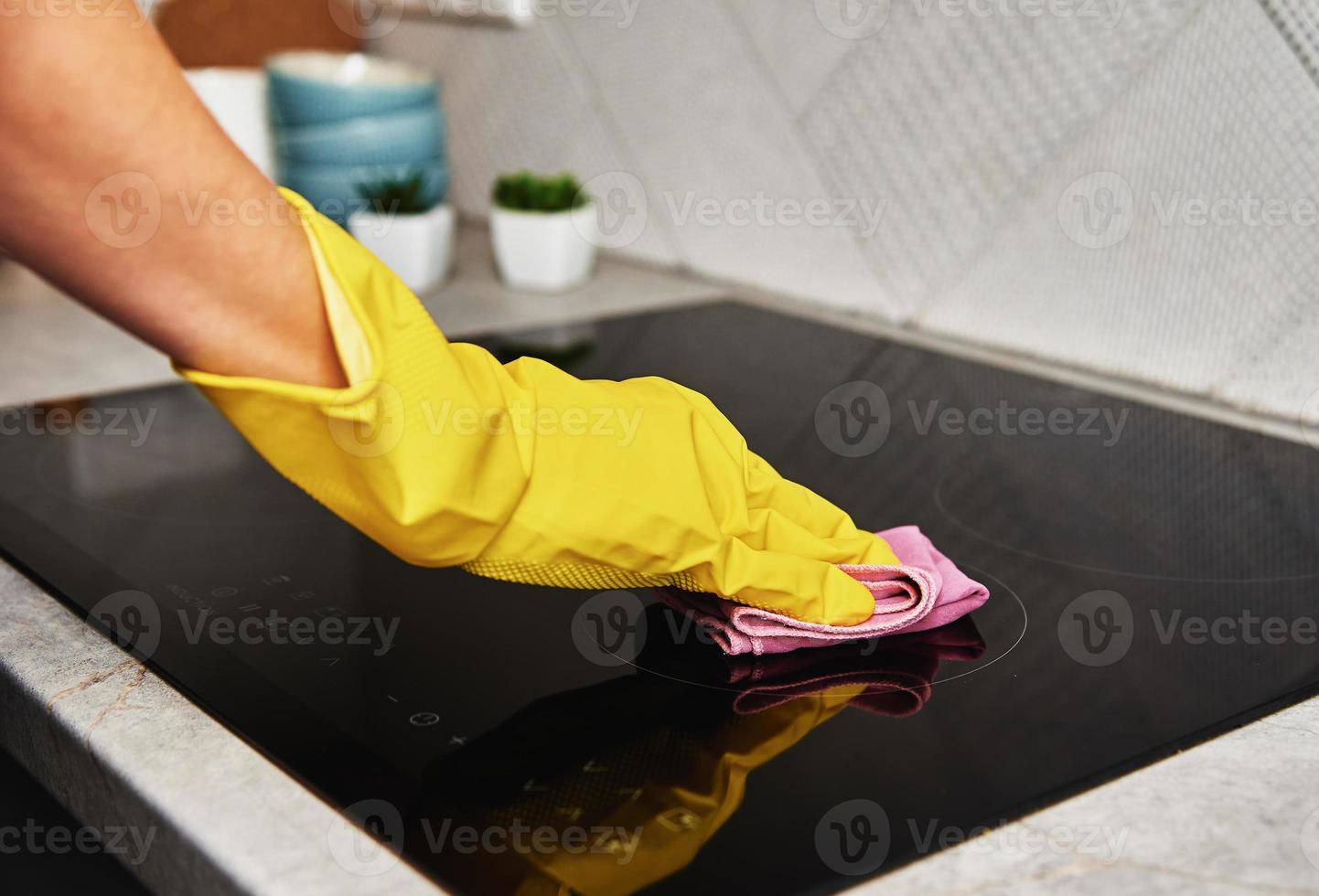mujer con guantes de goma limpiando estufa de inducción foto
