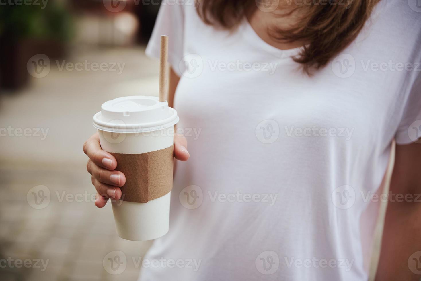 mujer sostiene una taza de café de papel en la calle de la ciudad foto
